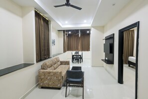 A modern living room with a sofa, chairs, a TV, and a ceiling fan. - Hotel Raaga Inn (Tirupati)