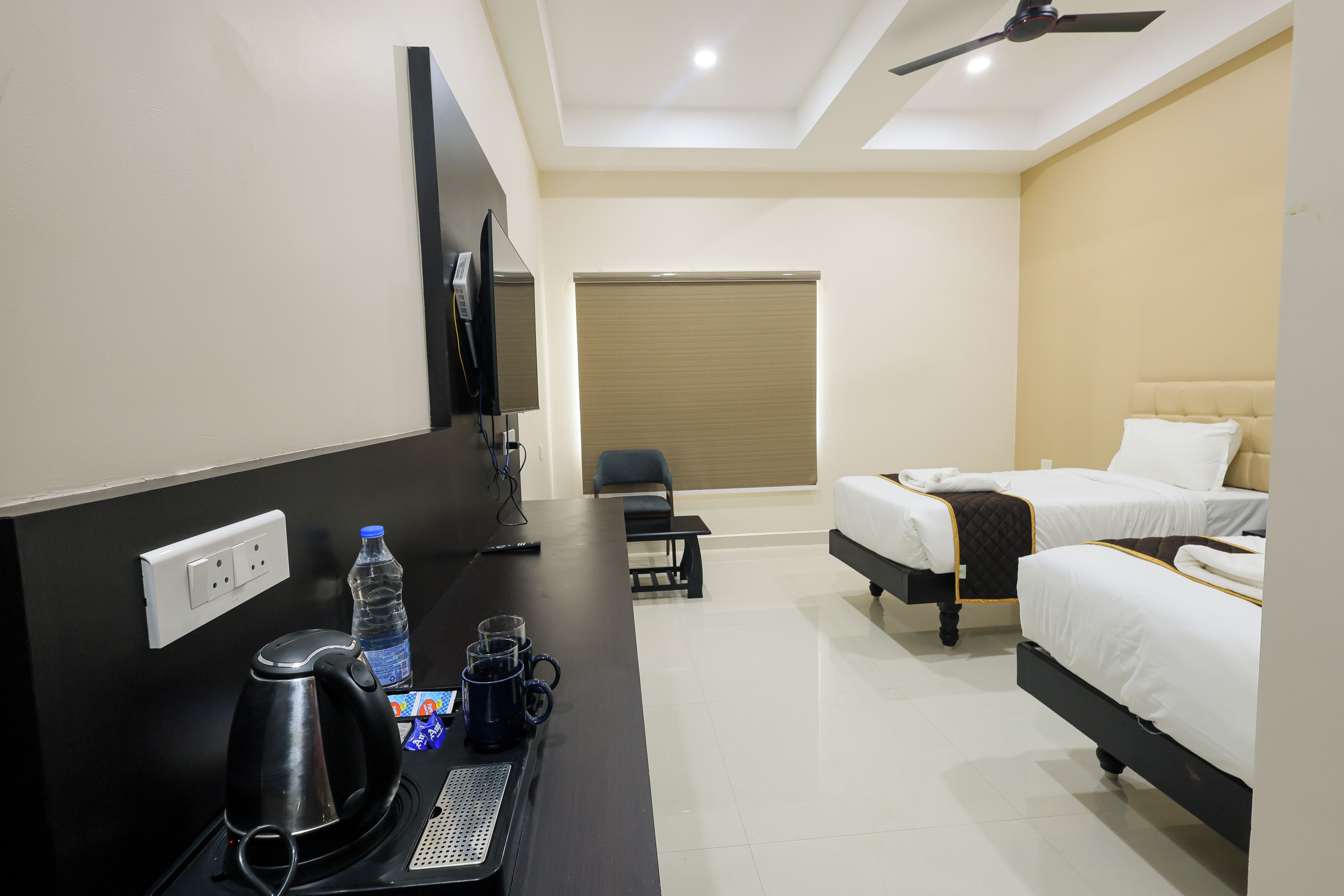 Una habitación de hotel con cama, escritorio con hervidor, televisor y ventana con persiana.