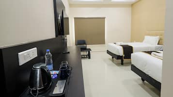 Una habitación de hotel con cama, escritorio con hervidor, televisor y ventana con persiana.