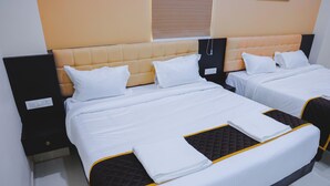 A hotel room with two beds, each with a headboard, white bedding, and a folded white towel on the beds. - Hotel Raaga Inn (Tirupati)