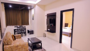 A living room with a sofa, a coffee table, a TV, and a dining area with chairs and a table. - Hotel Raaga Inn (Tirupati)