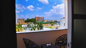 A balcony with two chairs and a small table, overlooking a cityscape with buildings and palm trees. - Hotel Raaga Inn (Tirupati)