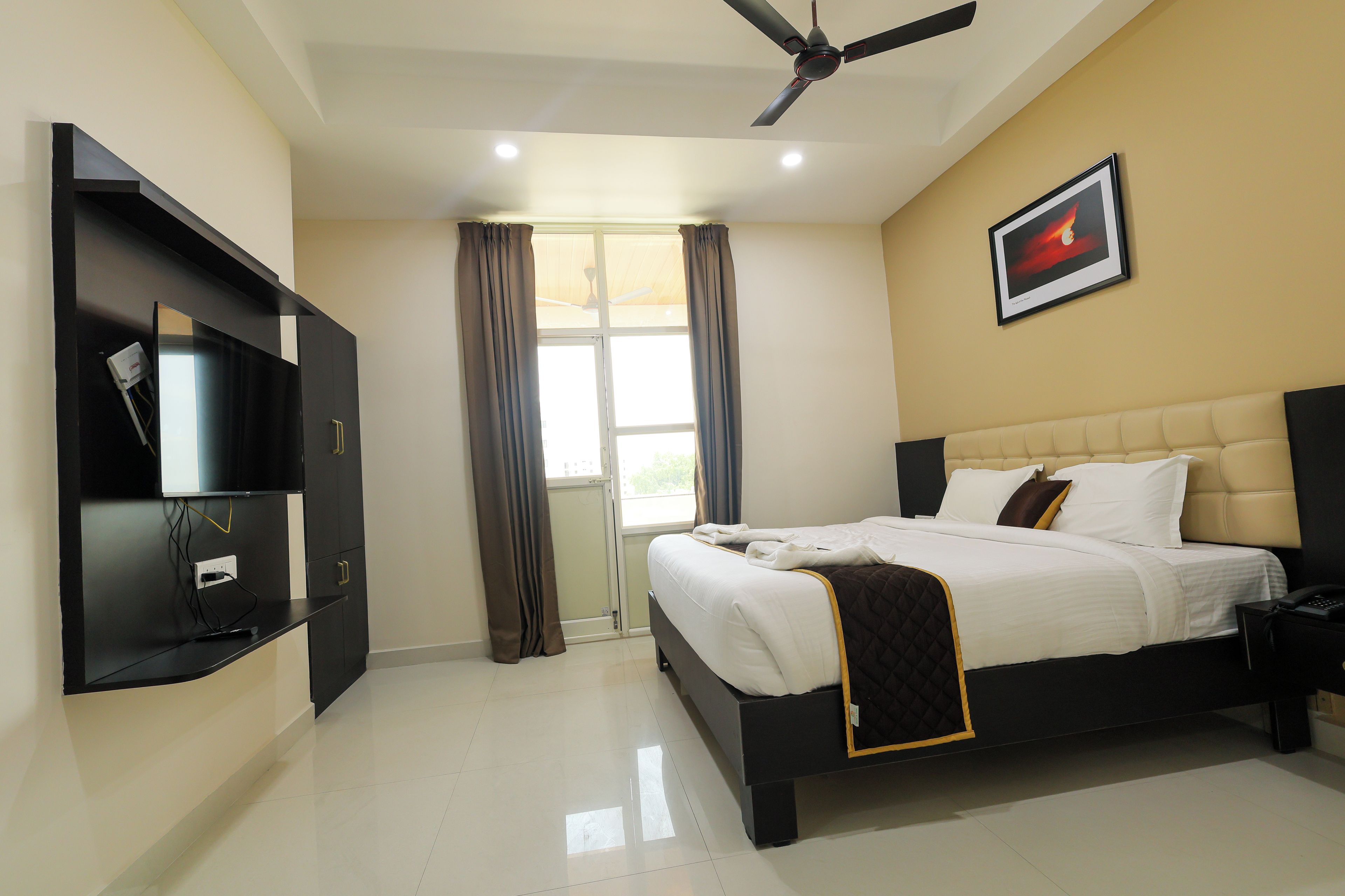 A hotel room with a bed, a television, a ceiling fan, and a window with curtains.