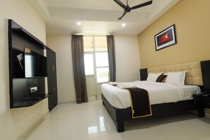 A hotel room with a bed, a television, a ceiling fan, and a window with curtains. - Hotel Raaga Inn (Tirupati)