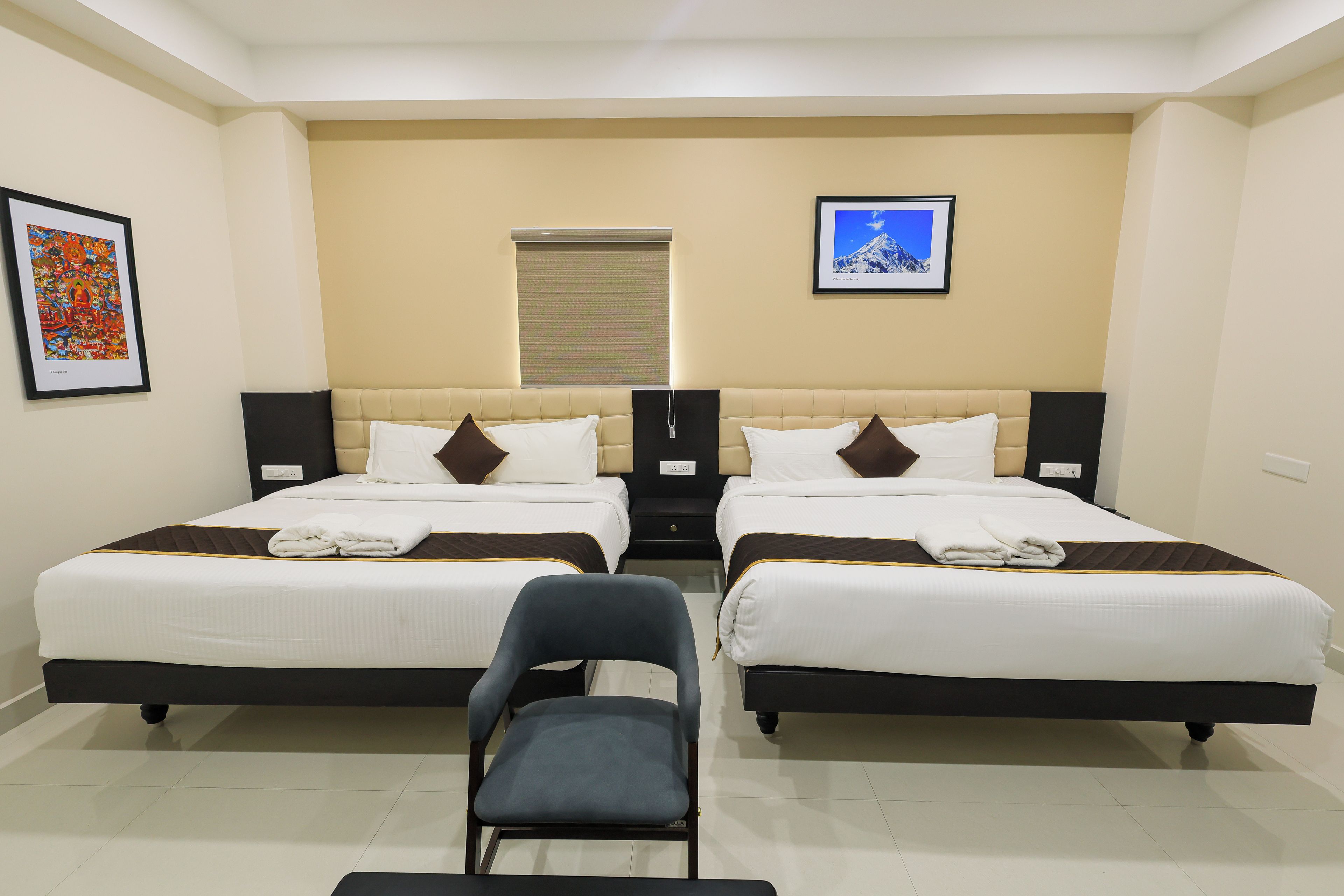 A hotel room with two beds, a chair, and artwork on the walls.