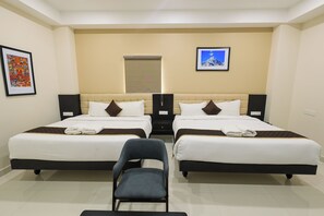 A hotel room with two beds, a chair, and artwork on the walls. - Hotel Raaga Inn (Tirupati)