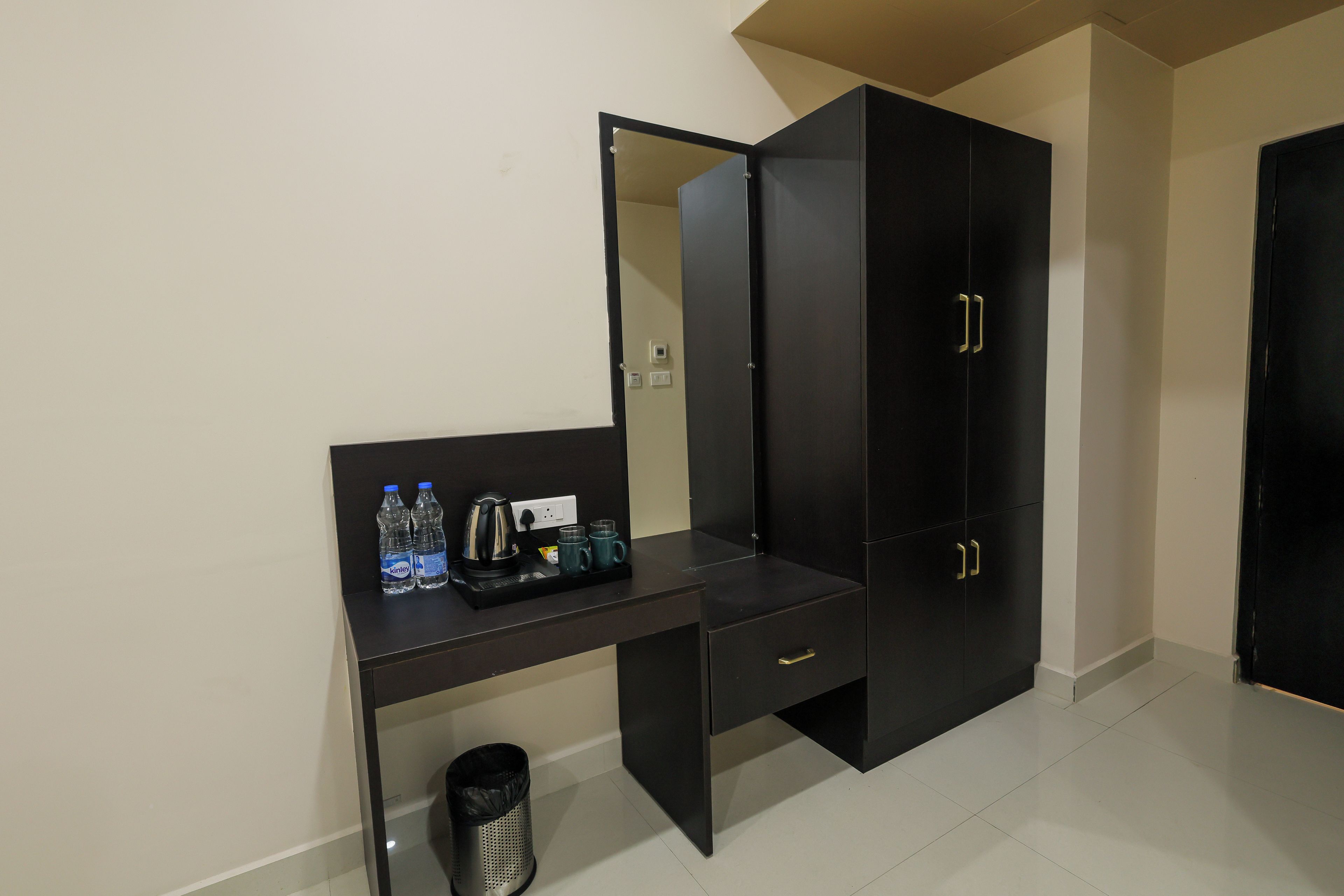 Una habitación con un escritorio negro, un cesto de basura, un dispensador de agua y una cafetera.