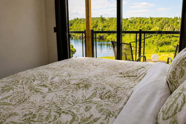 Ein Schlafzimmer mit Bett, Seeblick und einem Balkon mit Sitzgelegenheiten.