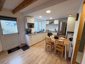 A compact kitchen with white cabinets, a wooden dining table, and a built-in oven. - Coastal Retreat for 4 With Terrace (Landunvez)
