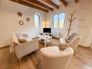 Un salon comprenant un canapé, un fauteuil, une table basse, un téléviseur et des œuvres d’art décoratives au mur.