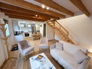 Un grand espace de vie comprenant un canapé, des fauteuils, une table basse et une cuisine en arrière-plan.