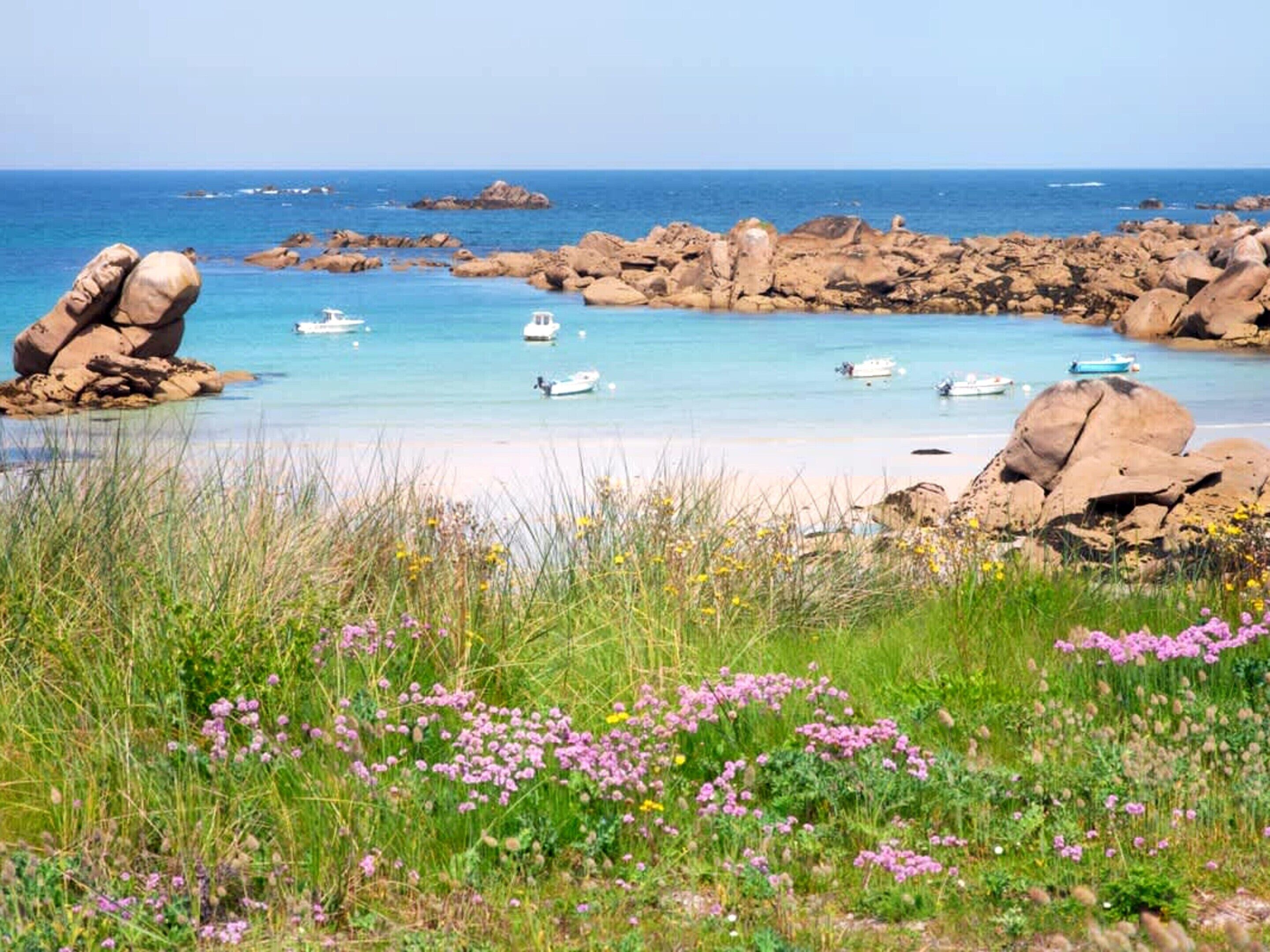 A coastal landscape with clear water, boats, and rocky formations.