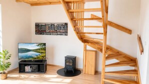 Uma sala de estar moderna com escada de madeira, televisão, lareira a lenha preta e uma pintura com vista para a cidade.