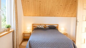 Uma cama de solteiro com cabeceira de madeira, duas mesas de cabeceira com abajures, uma janela com cortinas e piso de madeira.