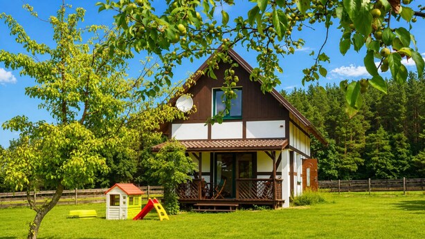 Uma casa de dois andares com varanda, um pequeno parquinho e um escorrega em um gramado.