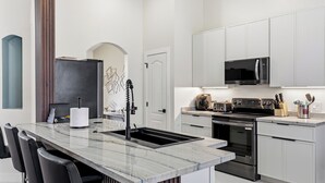Una cocina moderna con armarios blancos, una isla de mármol, horno empotrado y microondas.