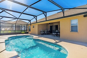 Une piscine entourée de parois en verre, des meubles de jardin et un espace salon couvert.