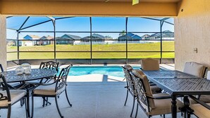 Un porche cubierto con piscina, mobiliario exterior y vistas a un barrio residencial.