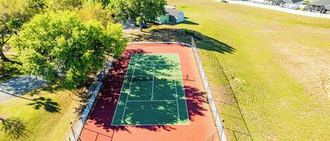 An aerial view of a tennis court surrounded by trees and residential buildings.