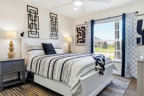 A neatly arranged bedroom with a bed, two bedside tables, a ceiling fan, and a large window with curtains. - Renovated 4BR Villa with Private Pool (Davenport)