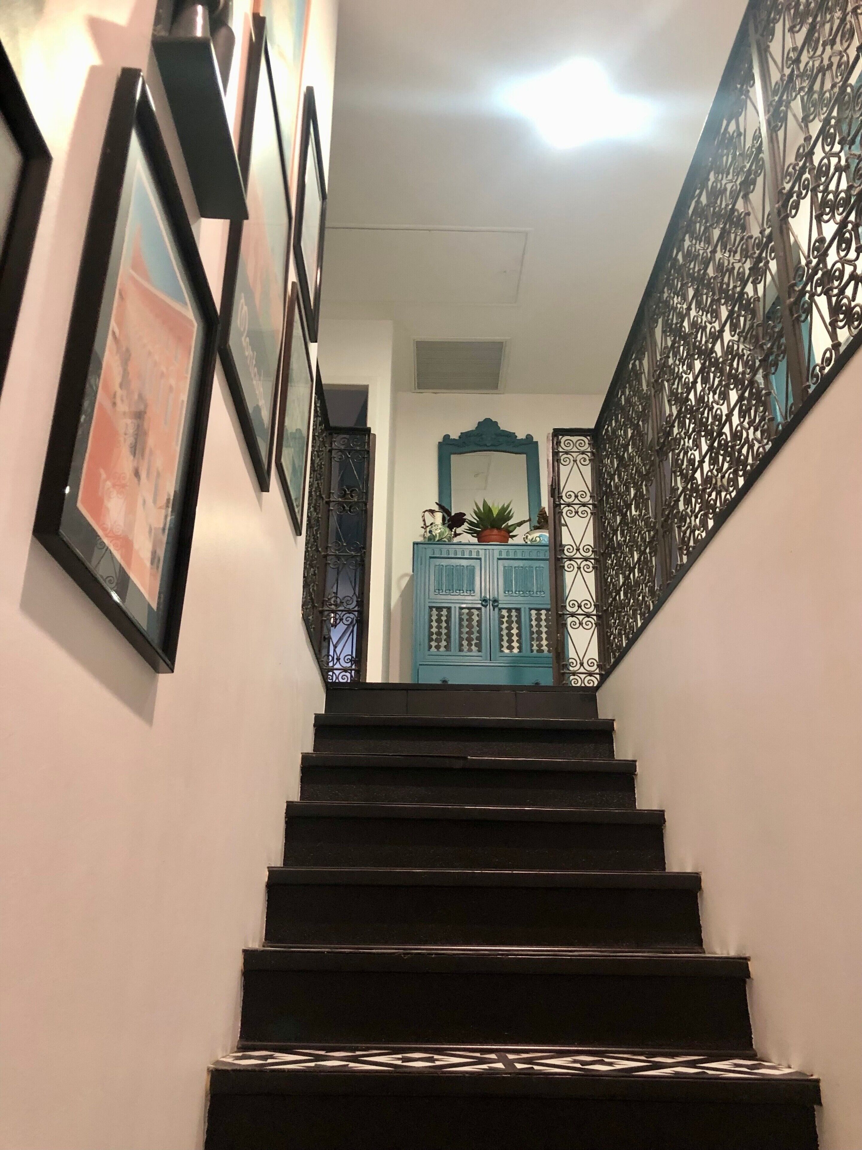 Una escalera con un armario azul en la parte superior, rodeada de barandillas negras y cuadros en las paredes.