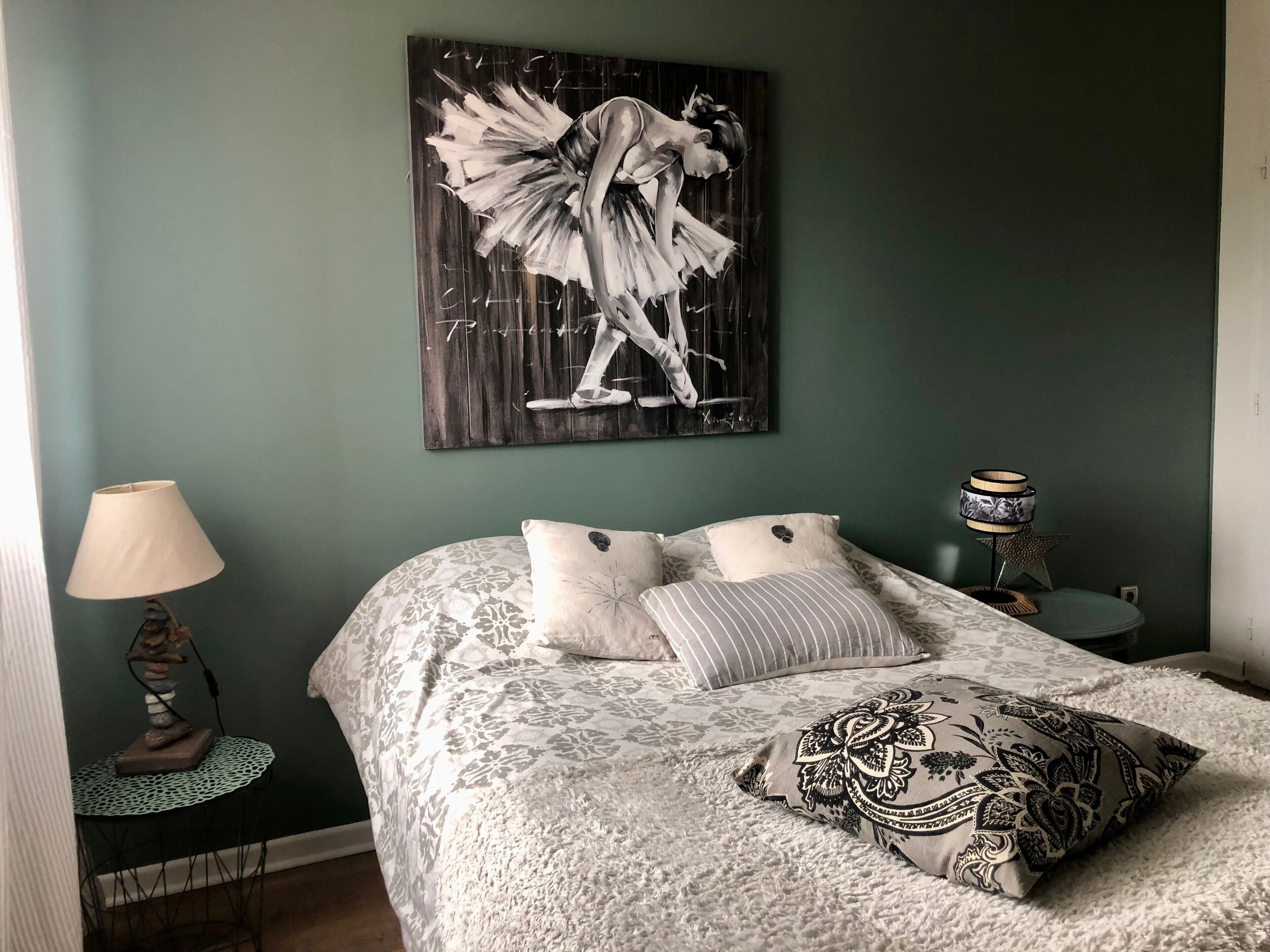 Un dormitorio con cama, almohadas, una mesita de noche, una lámpara y una obra de arte en la pared.