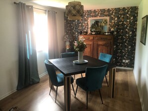 Un comedor con una mesa de madera, cuatro sillas, un jarrón con flores, un aparador con adornos y un papel tapiz floral.