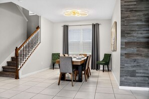 A dining area with a wooden staircase, a dining table with chairs, and a window with curtains. - 7BR Solara Resort Villa with Private Pool, Spa & Game Room (Kissimmee)