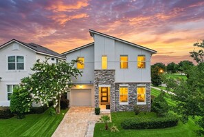 A modern two-story house with a stone facade, a garage, and a well-maintained lawn. - 7BR Solara Resort Villa with Private Pool, Spa & Game Room (Kissimmee)