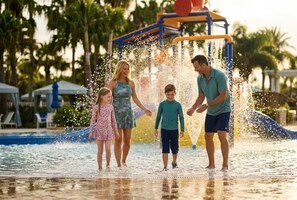A water play area with a slide and water jets, surrounded by palm trees and a pool. - 7BR Solara Resort Villa with Private Pool, Spa & Game Room (Kissimmee)