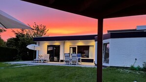 Uma casa moderna com alpendre coberto, gramado e vista para o pôr do sol.