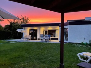 A modern house with a covered patio, a lawn, and a sunset view. - 6-person Bungalow in Burgerbrug (Nieuwvliet)