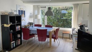 Uma sala de jantar com mesa, cadeiras, estante, televisão e janela com vista para o verde.