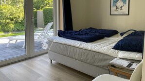 Quarto com cama, janela, quadro e vista para o verde lá fora.