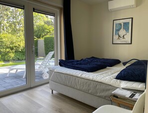 A bedroom with a bed, a window, a painting, and a view of greenery outside. - 6-person Bungalow in Burgerbrug (Nieuwvliet)