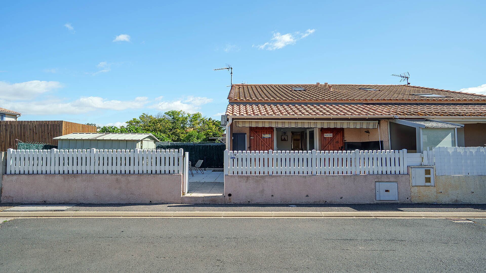A single-story house with a tiled roof, a white picket fence, and a small porch.