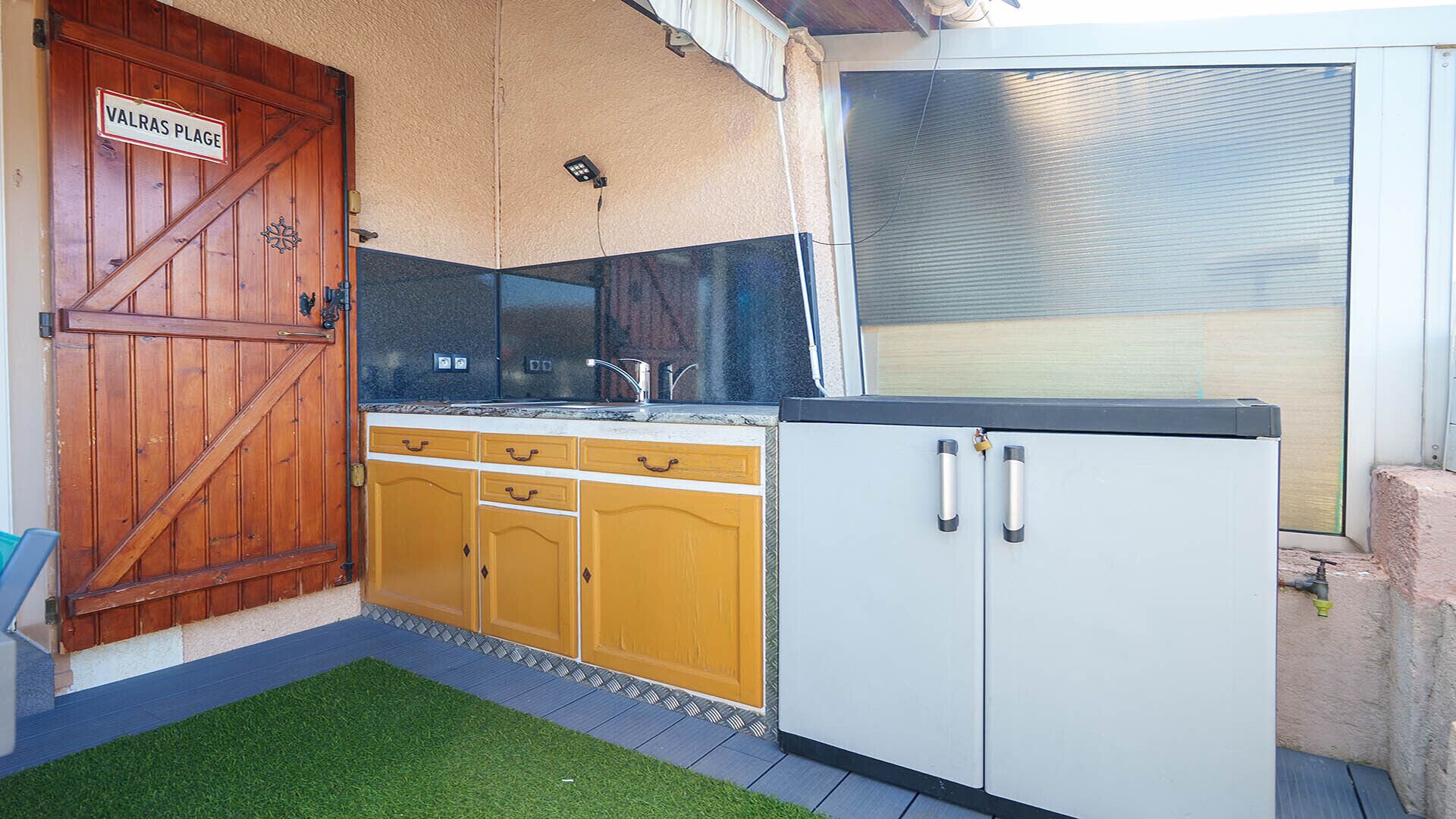 A kitchen with a wooden door labeled 'VALRAS PLAGE,' a sink, and a white cabinet.