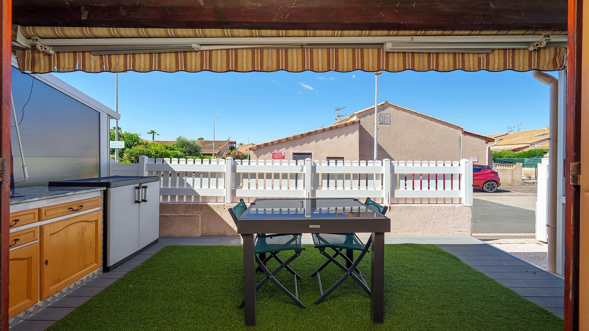 A patio with a table and chairs, a white fence, and a building in the background.