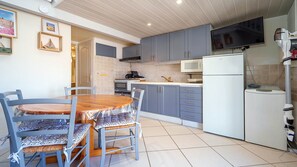 A compact kitchen with grey cabinets, a white refrigerator, and a dining area with a wooden table and blue chairs. - Bright duplex apartment - sleeps 5 (Valras-Plage)