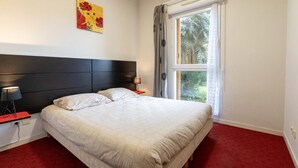 Une chambre à coucher comprenant un lit, deux tables de chevet, une commode, une fenêtre avec des rideaux et une œuvre d’art murale.