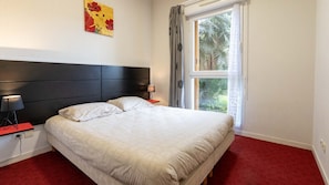 Ein Schlafzimmer mit einem Bett, zwei Nachttischen, einem Fenster mit Vorhängen und einem Wandbild.