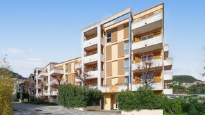 Un immeuble r ésidentiel à plusieurs étages, doté de balcons, d’une entrée pavée et entouré de verdure.