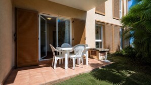 Une terrasse avec une table et des chaises, une porte-fenêtre coulissante et un petit jardin.
