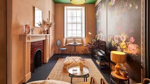 Un cuarto acogedor con chimenea, una mesa redonda, una lámpara, un piano y un mural floral.