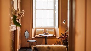 Una habitación acogedora con un asiento junto a la ventana, una mesita, un espejo y una planta en maceta.
