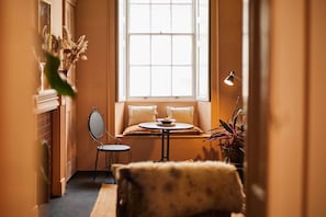 A cozy room with a window seat, a small table, a mirror, and a potted plant.