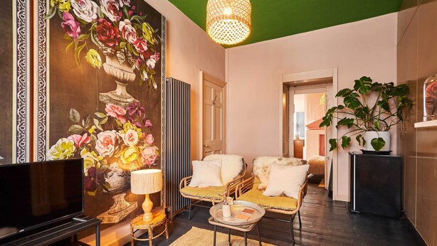 Una sala de estar con televisor, mobiliario de mimbre, un adorno mural y techo verde.