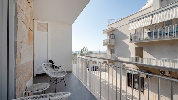 A balcony with wicker chairs, a white door, and a view of the street.