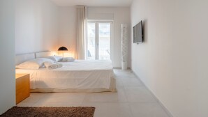 A hotel room with a bed, a desk, a lamp, a TV, and a window with curtains.