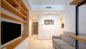 A modern living room with a flat-screen TV, wooden shelves, a gray sofa, and a wall-mounted artwork.
